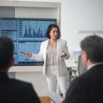 Professional woman presenting stock market data in a modern office setting.
